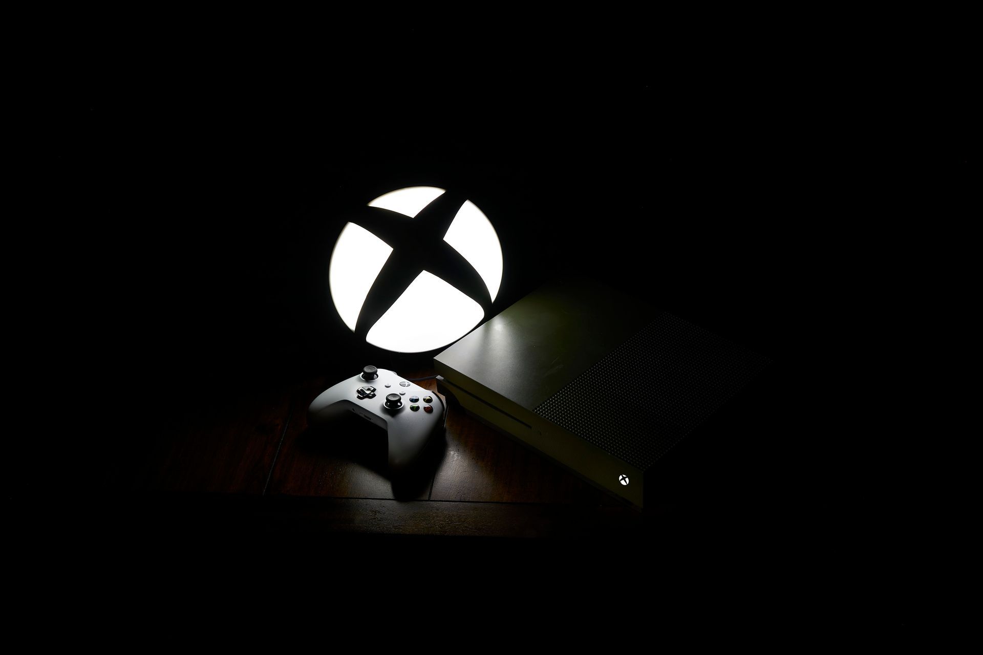 A xbox controller is sitting on top of an xbox console in the dark.
