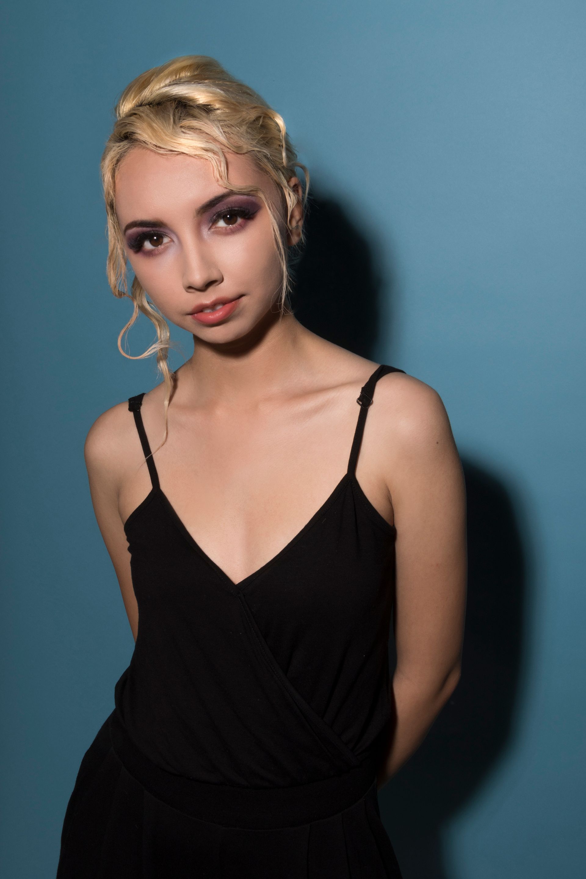 A woman in a black dress is standing in front of a blue wall.
