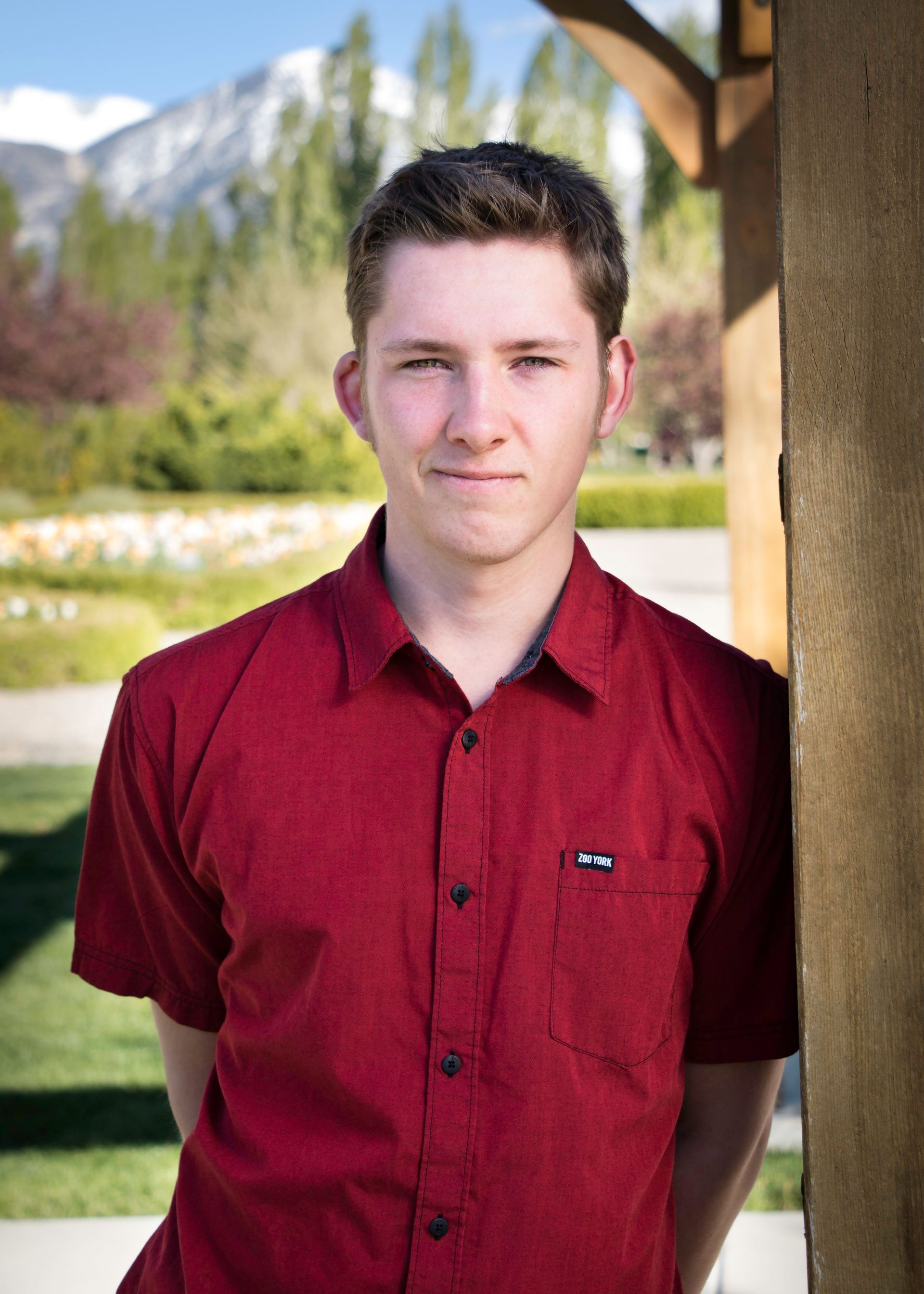 A young man in a red shirt is leaning against a wall.