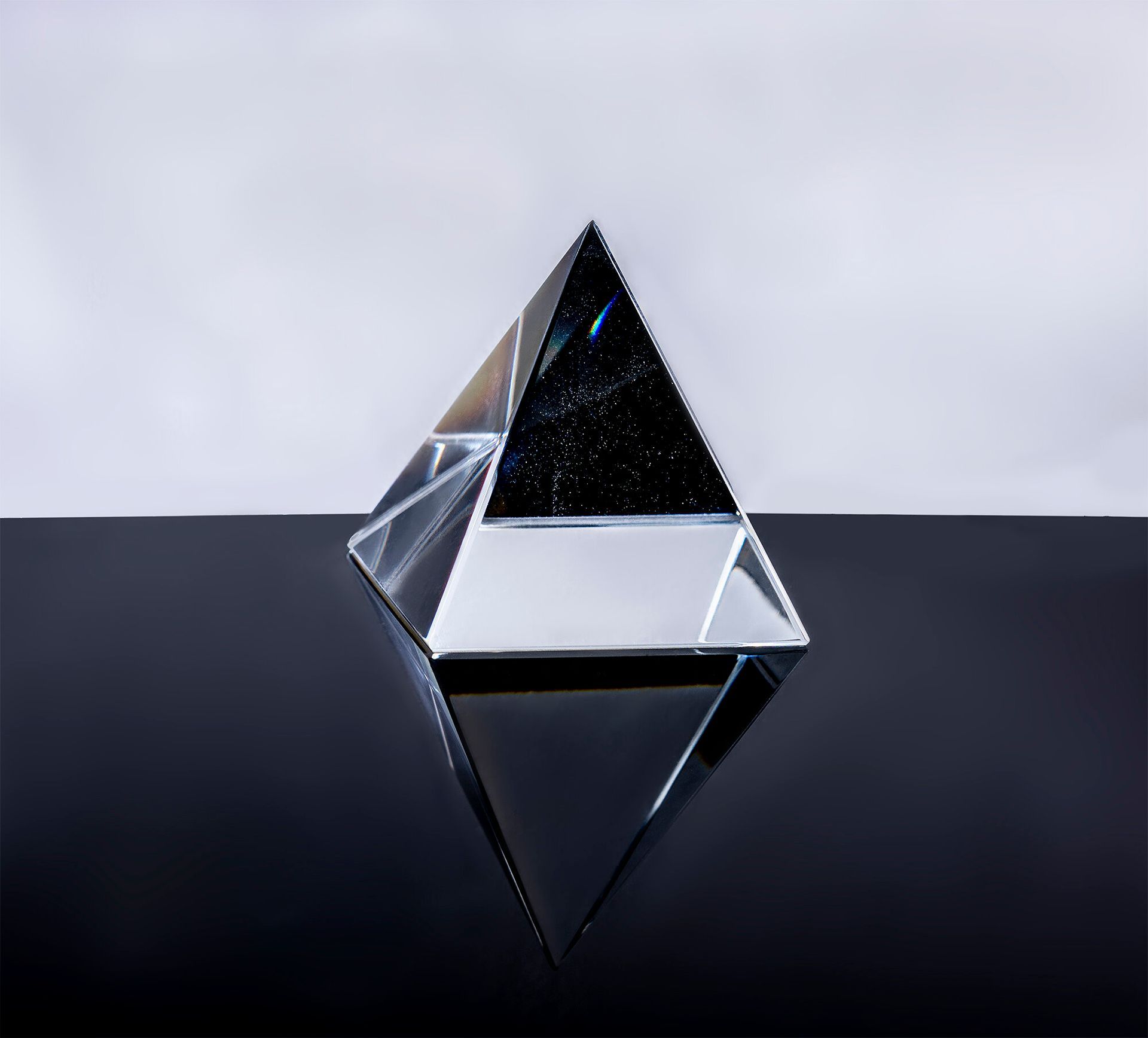 A clear glass pyramid is sitting on a black surface.