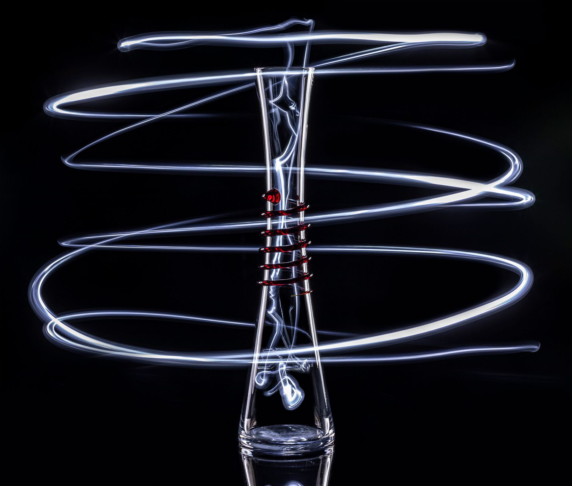 A light swirls around a glass bottle on a black background