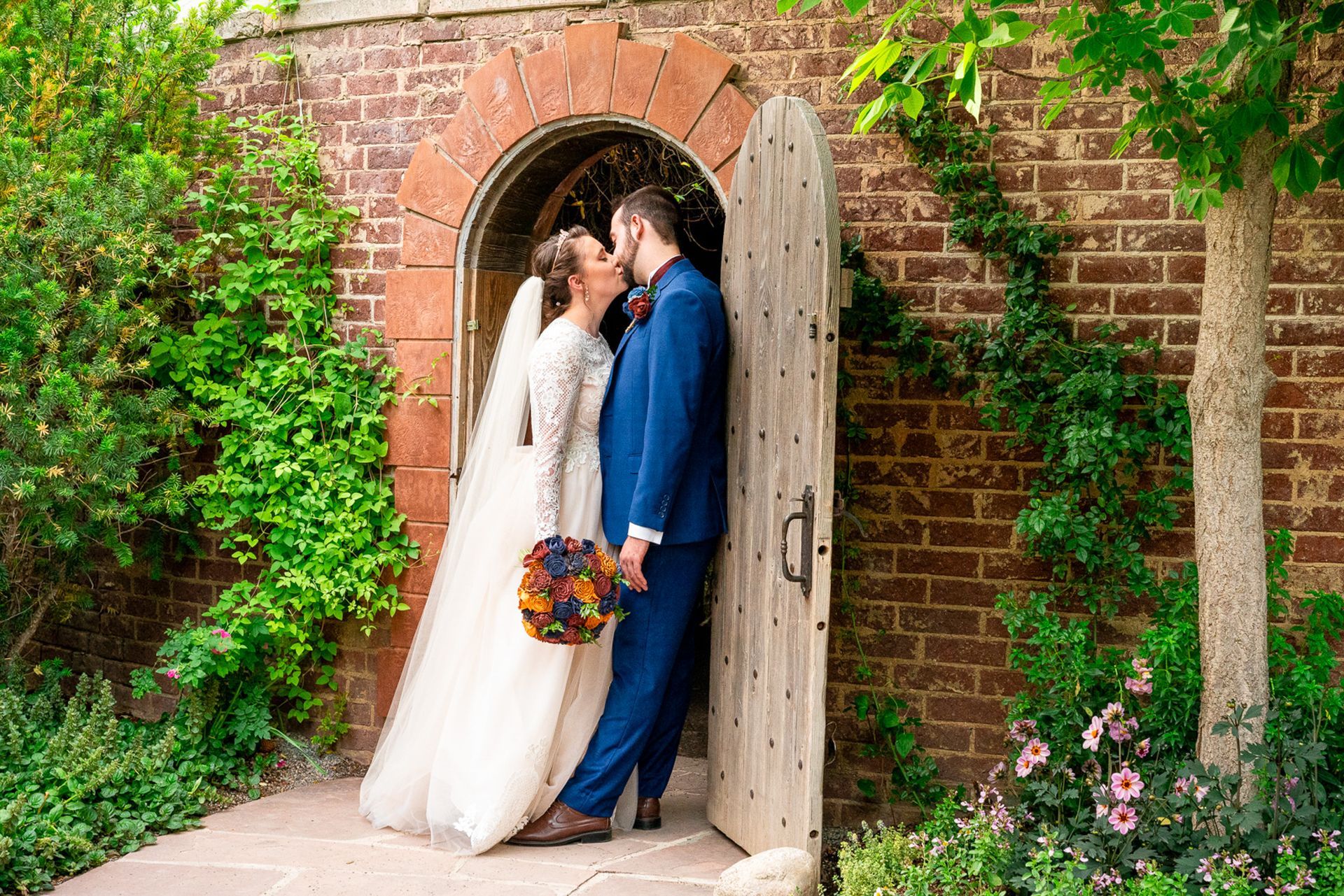 A bride and groom are kissing in front of a wooden door.