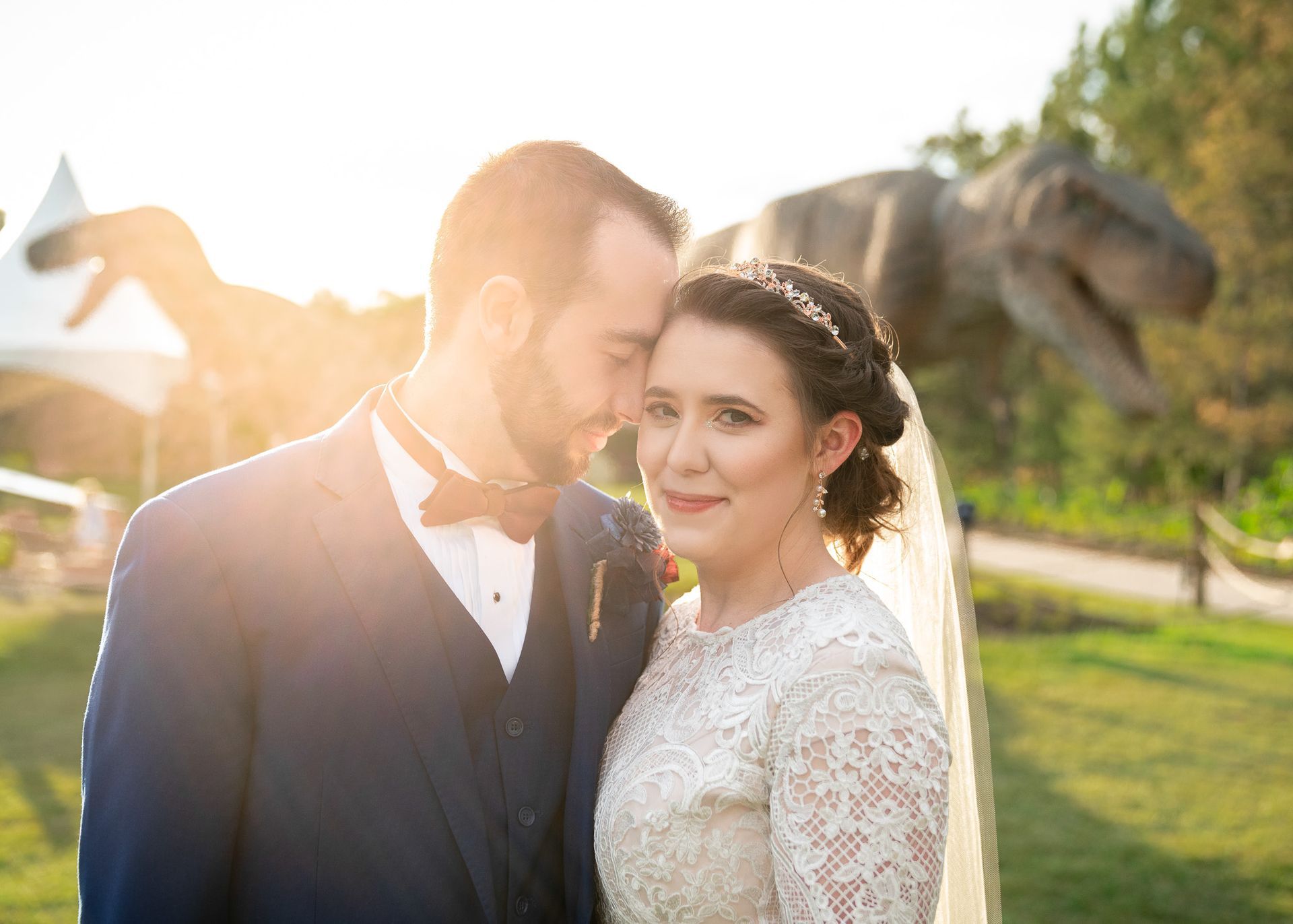 A bride and groom are posing for a picture in front of a dinosaur statue.