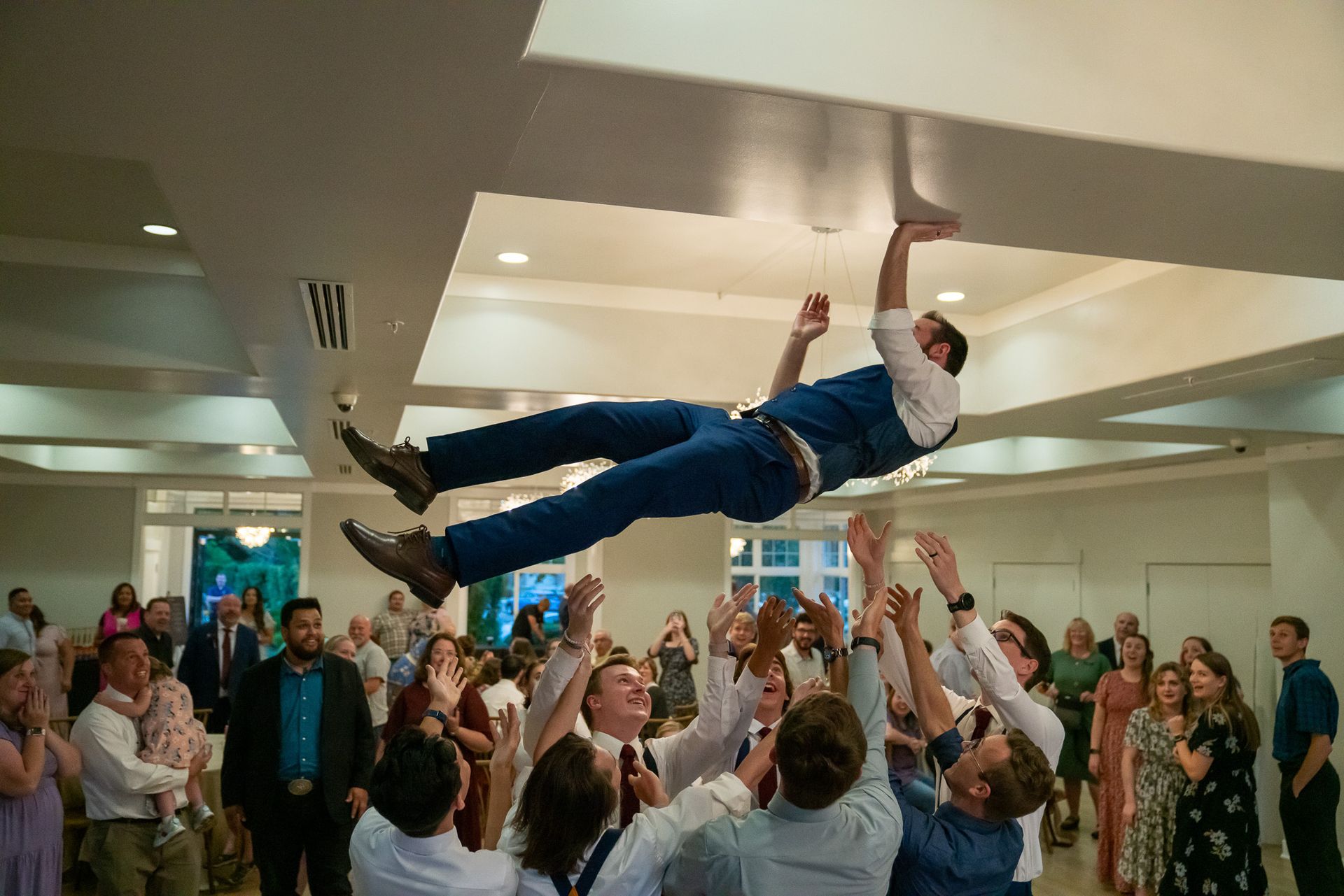 A man is being tossed in the air by a group of people at a wedding reception.