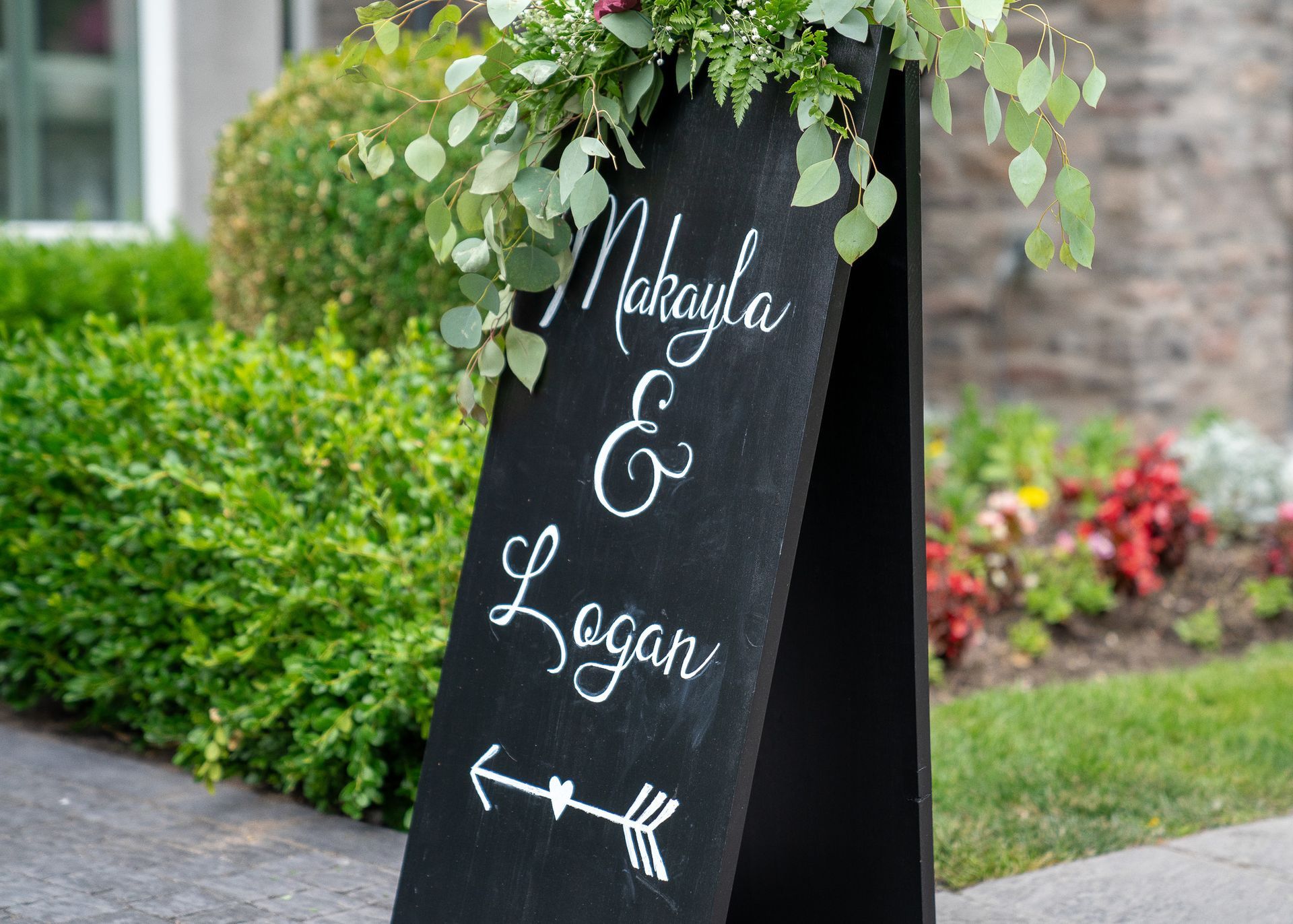 A black sign with flowers on it is sitting on the sidewalk in front of a house.