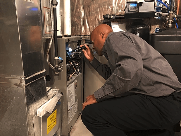 A man is kneeling down in a basement looking at a furnace.