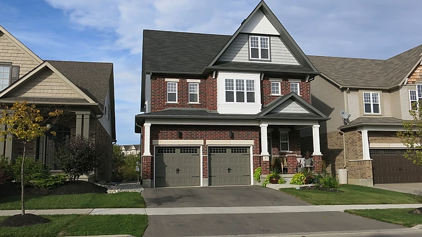 A large brick house with two garages is sitting next to a smaller house.