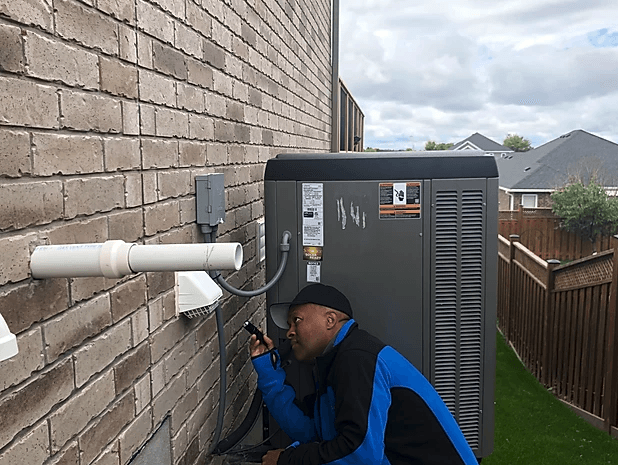 A man is working on an air conditioner on the side of a brick building.