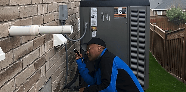 A man is working on an air conditioner on a brick wall.