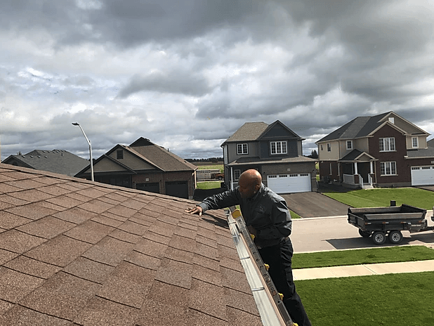 A man is standing on top of a roof in a residential area.