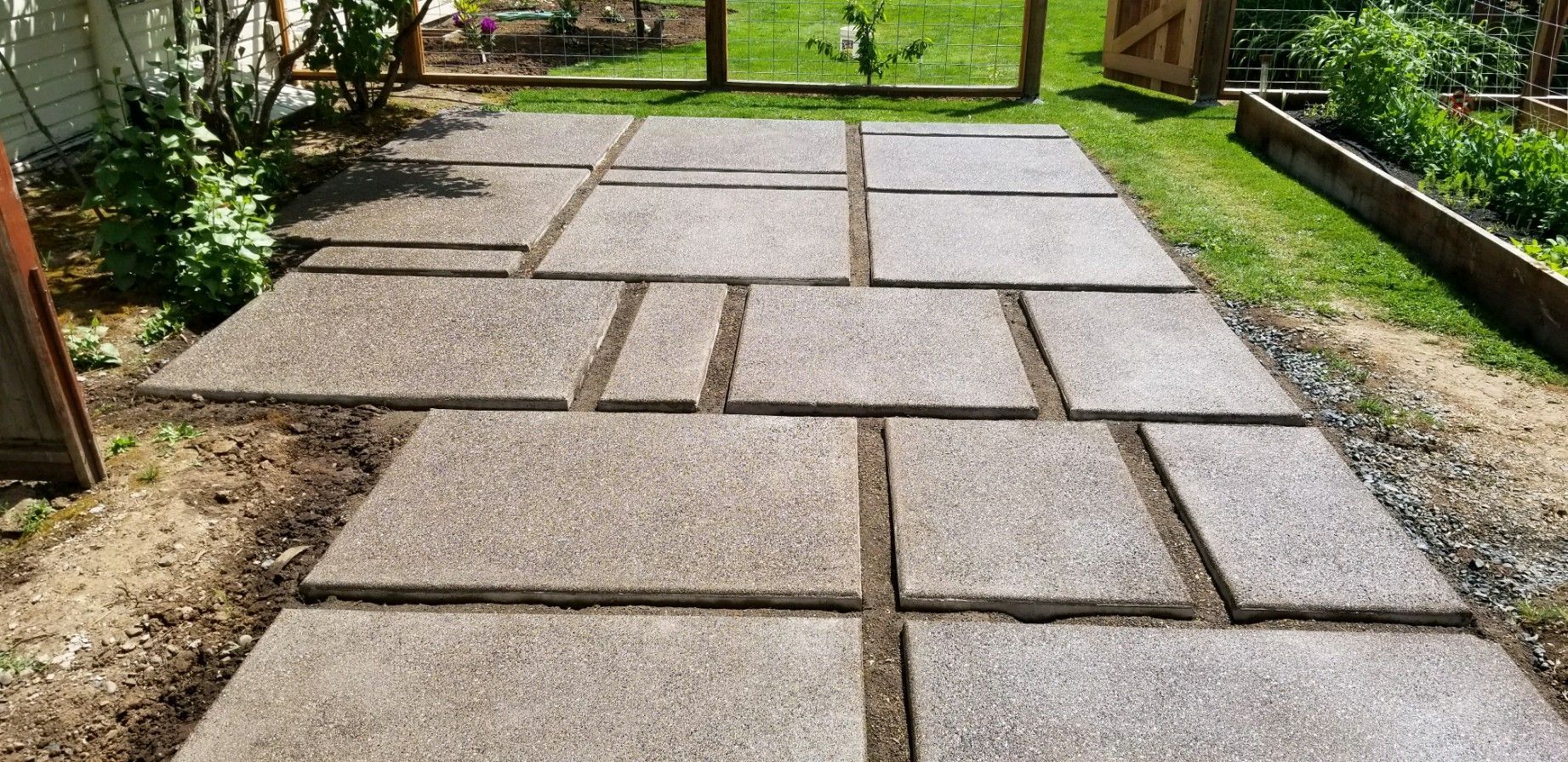 A concrete walkway in a backyard with a fence in the background.