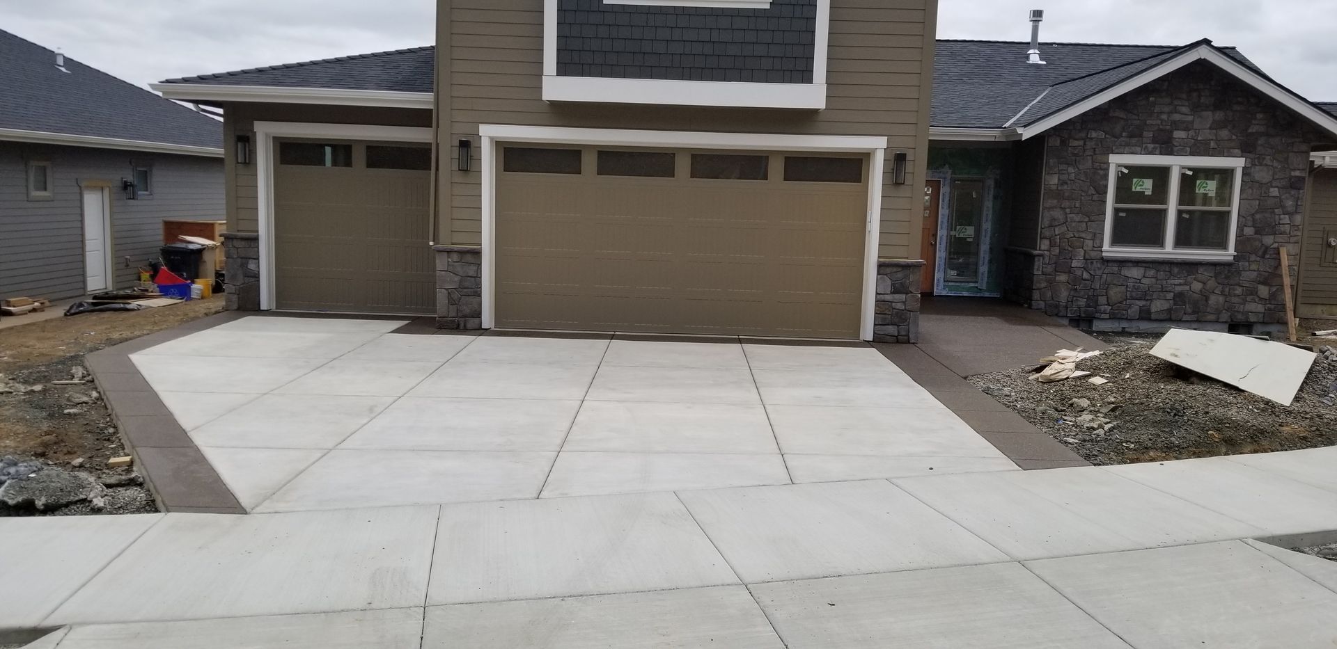 A house with two garage doors and a concrete driveway in front of it.