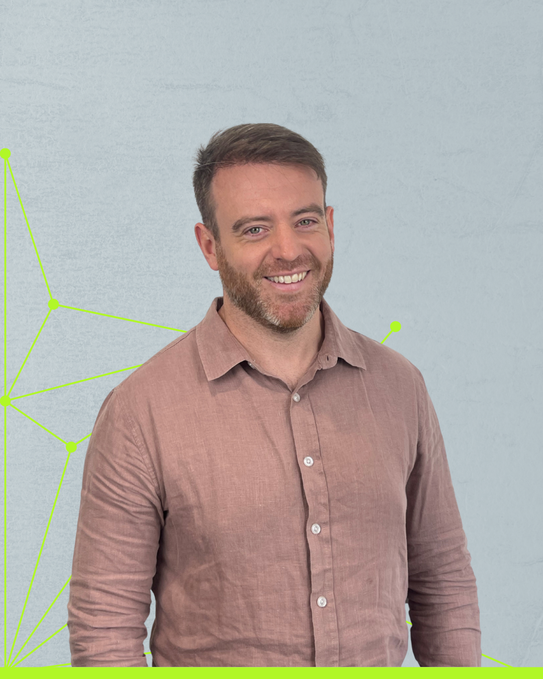 Smiling man in a pink shirt standing against a light gray wall