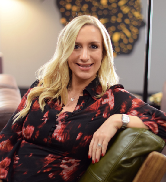 Blonde woman in a red-and-black blouse smiling on a green couch in a modern lounge