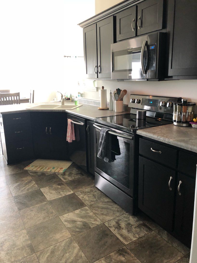a kitchen with black cabinets , a stove , a microwave , and a sink .