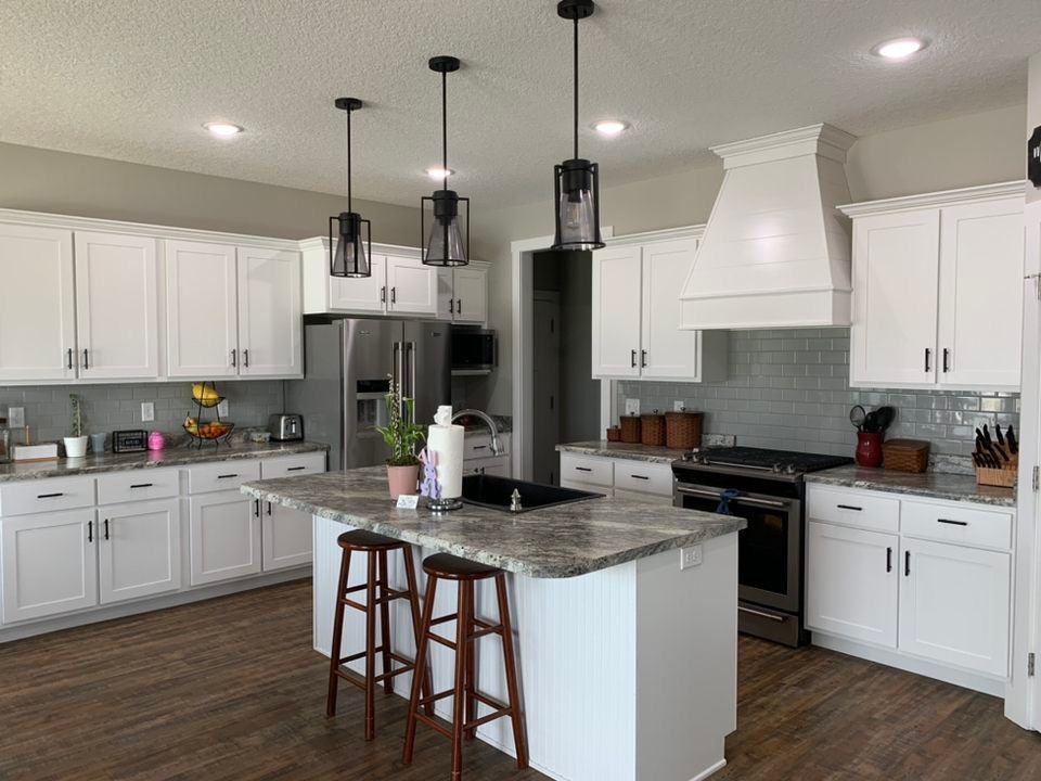 a kitchen with white cabinets , granite counter tops , stainless steel appliances and a large island .