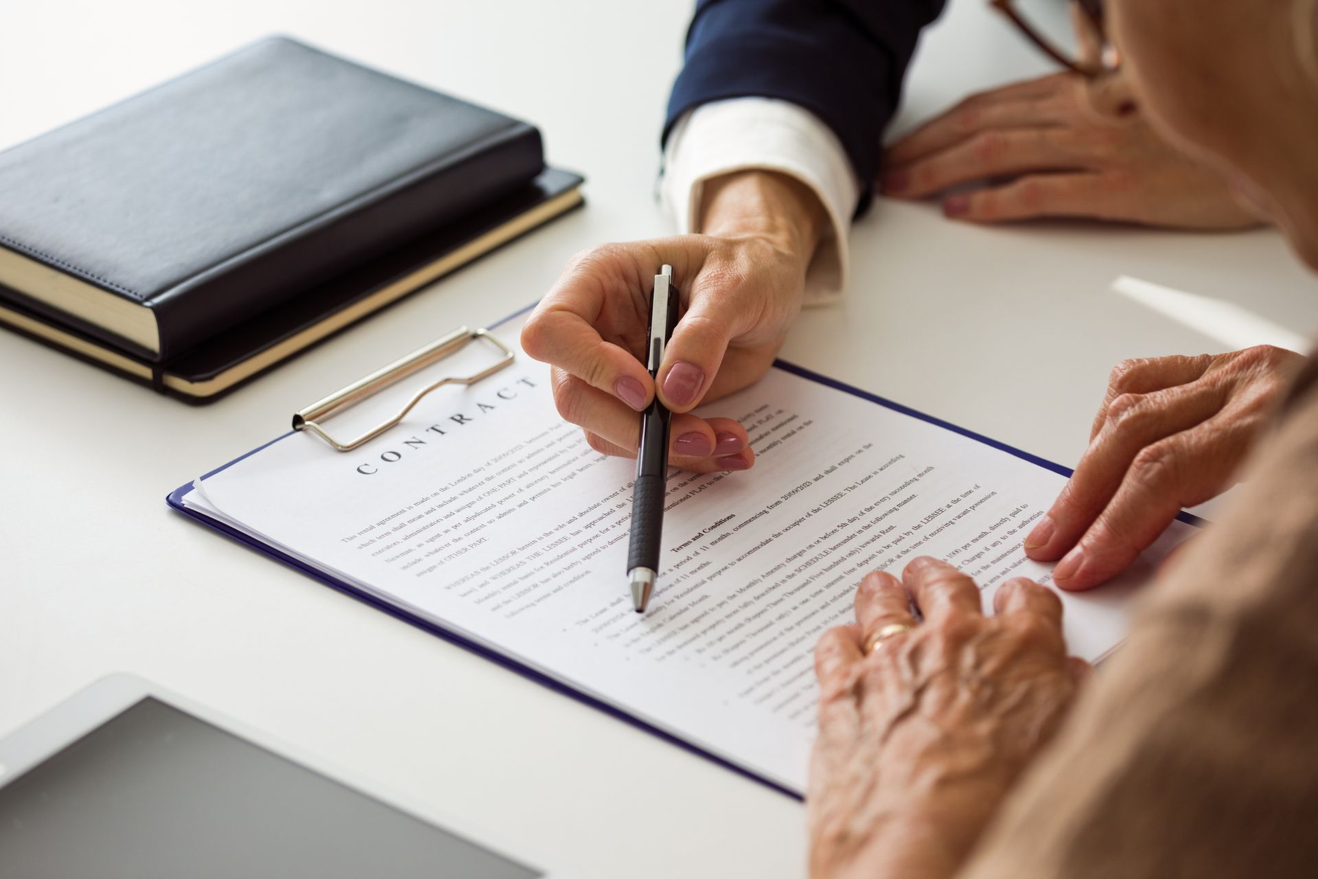 Close-up of female solicitor hands, explaining contract details to senior woman. Close-up of female solicitor hands, explaining contract details to senior woman.
