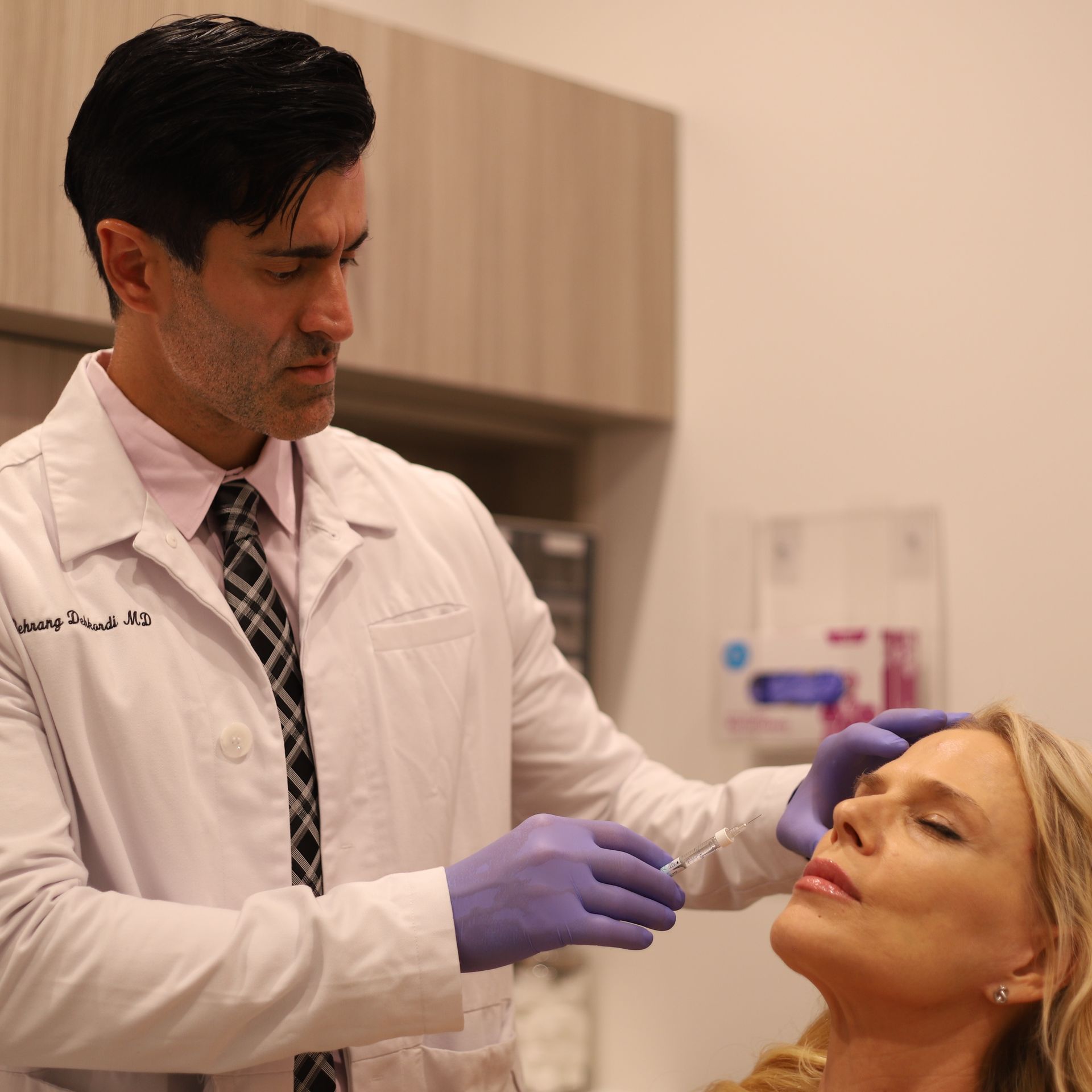 A man in a white coat and purple gloves is examining a woman 's face