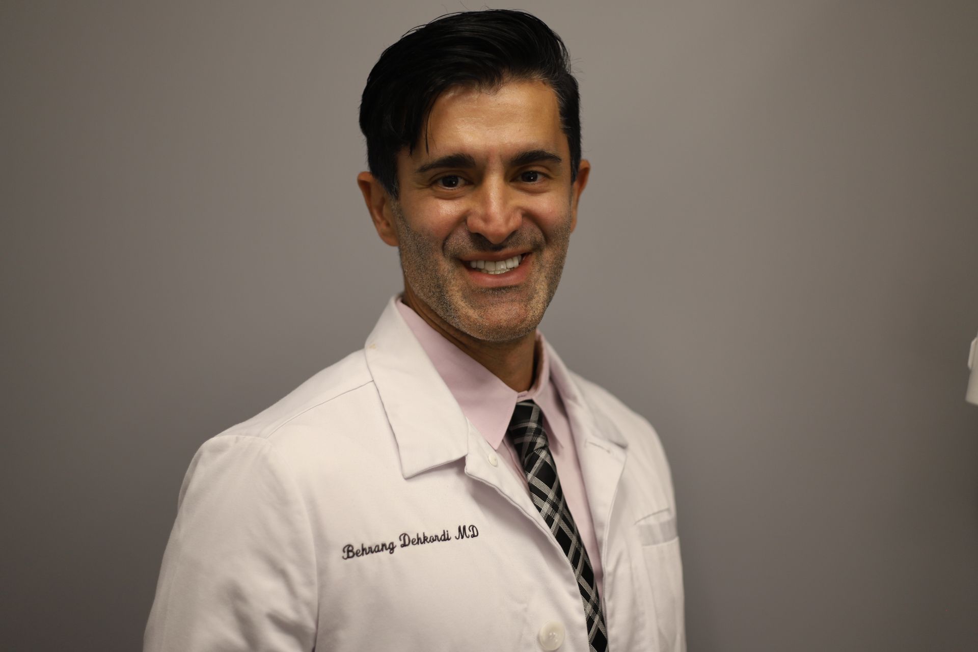 A man in a white coat and tie is smiling for the camera.