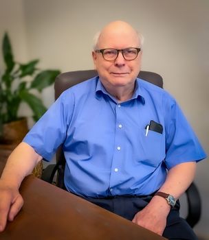 A man in a blue shirt and glasses is sitting at a desk