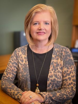 A woman in a leopard print sweater is sitting at a desk with her hands folded.
