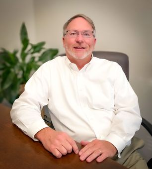 A man in a white shirt and glasses is sitting at a table.