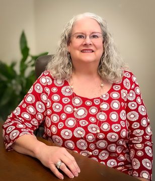 A woman in a red and white polka dot shirt is sitting at a desk.
