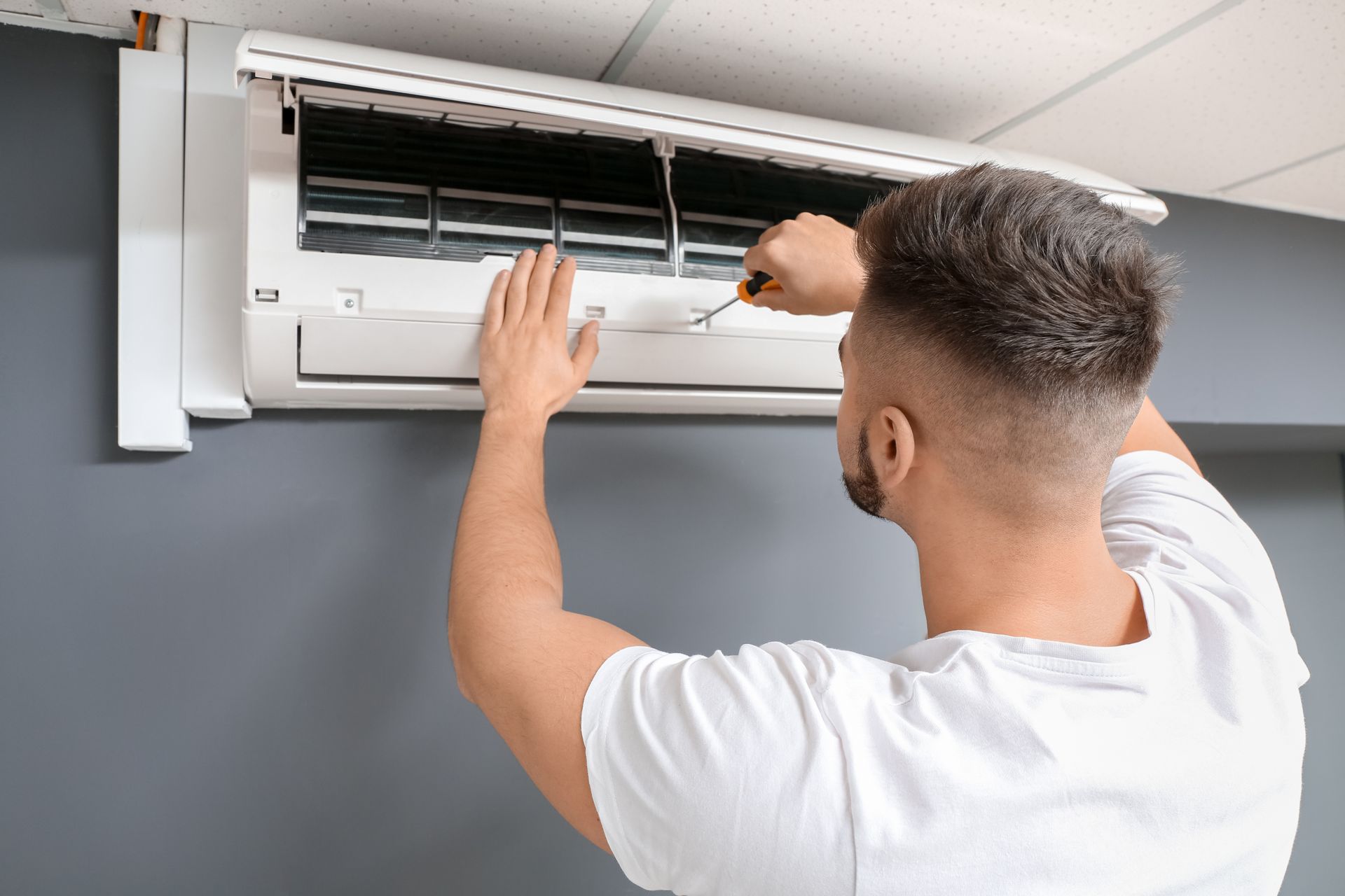 Contractor using a screwdriver to service an indoor air conditioning unit mounted on the wall.