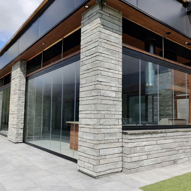 Angolo di un edificio moderno con pareti vetrate a tutta altezza e colonne in mattoni chiari sotto una tettoia in legno.