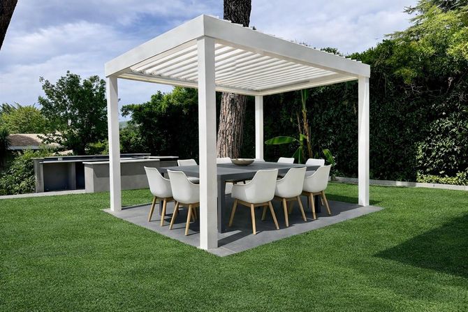Zona pranzo esterna con pergola bianca, tavolo e sedie su un rigoglioso prato verde.