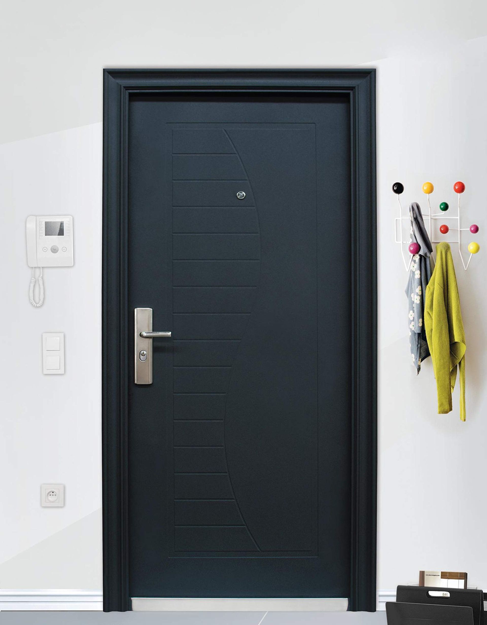 In un ingresso bianco, la porta d'ingresso è scura, con maniglia argentata e ganci colorati a parete per appendere i cappotti.