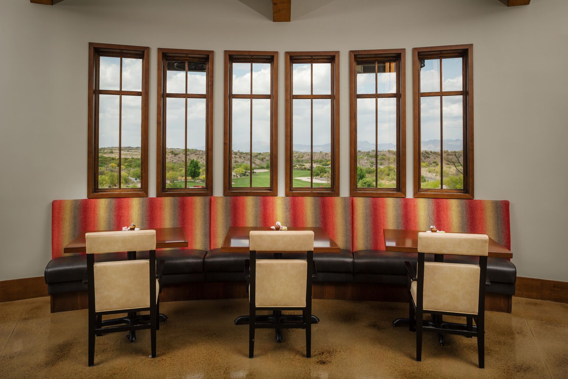 A dining room with tables and chairs and a bench with a view of a golf course.