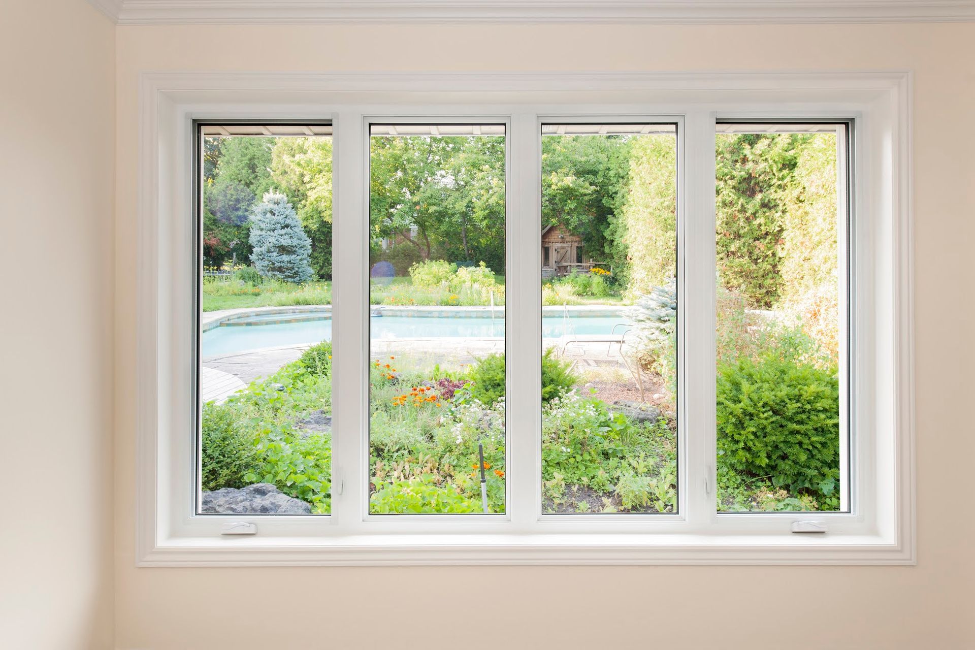 White-framed window overlooking a lush green garden with a swimming pool.