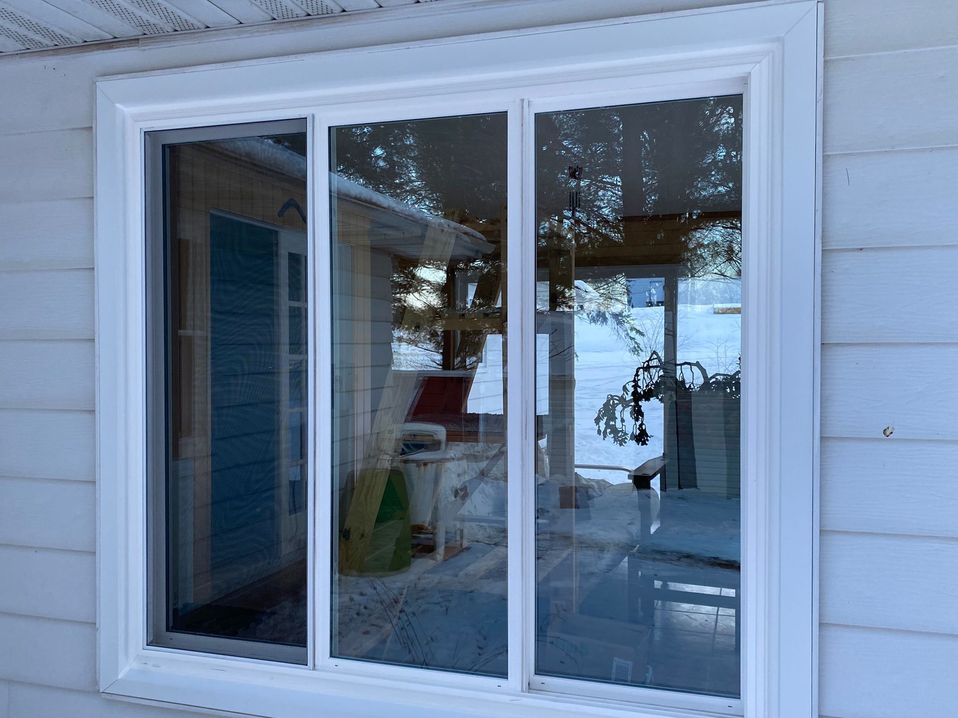 White-framed sliding glass window on a light blue house exterior, reflecting outdoor scene with snow.