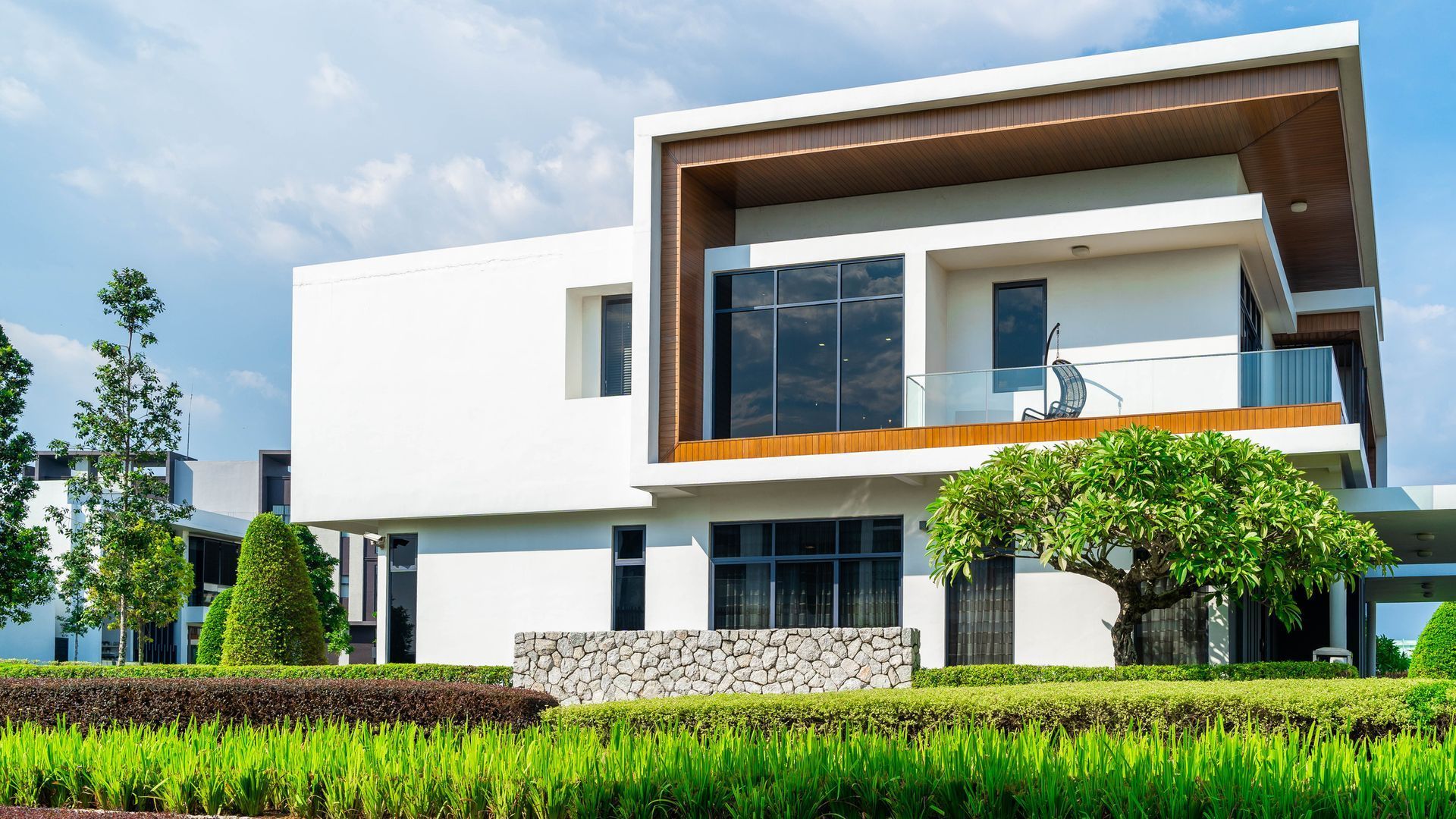Modern white two-story house with dark windows, wooden accents, and manicured green landscaping.