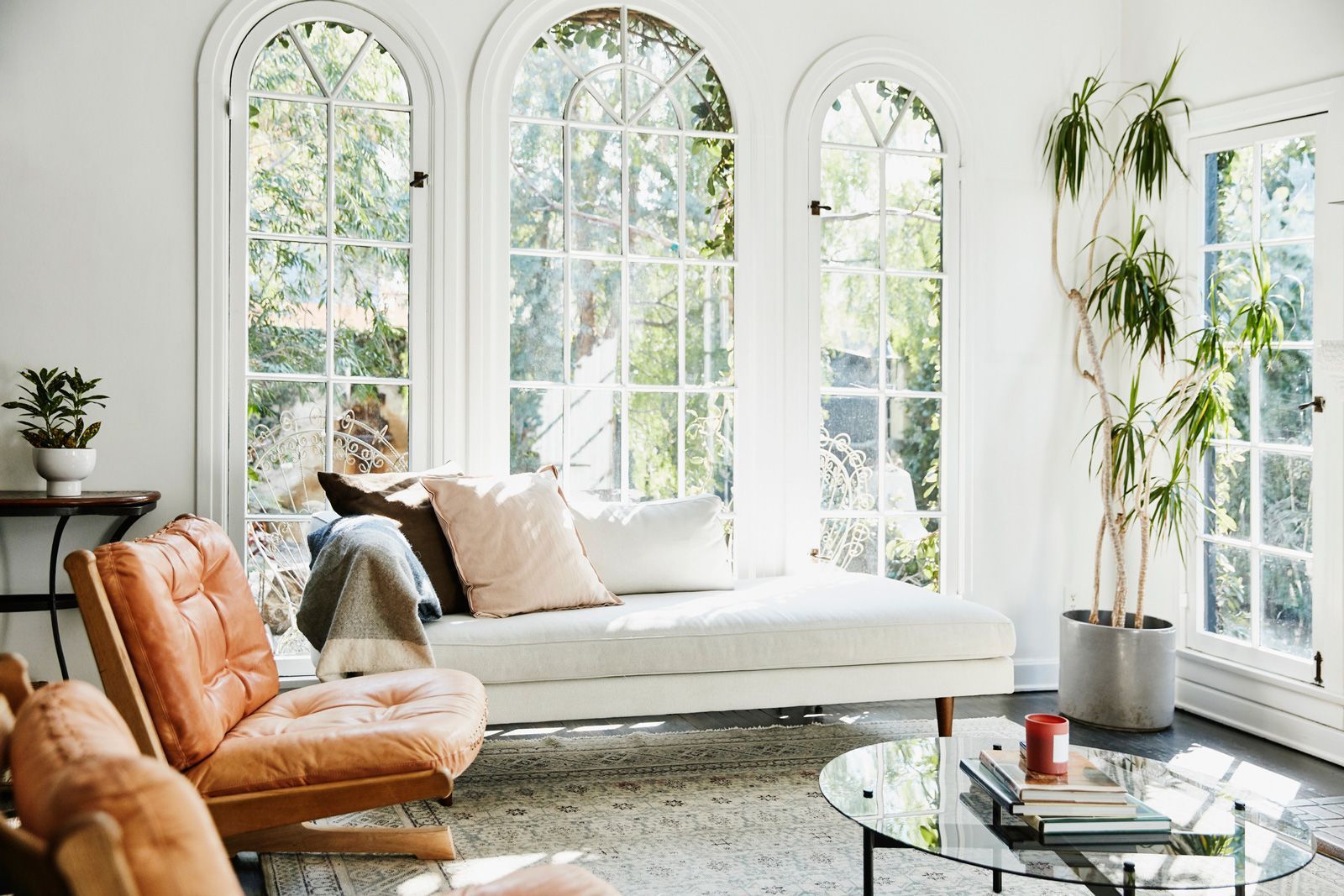 Bright living room with arched windows, light-colored sofa, leather chair, potted plant, and a glass coffee table.