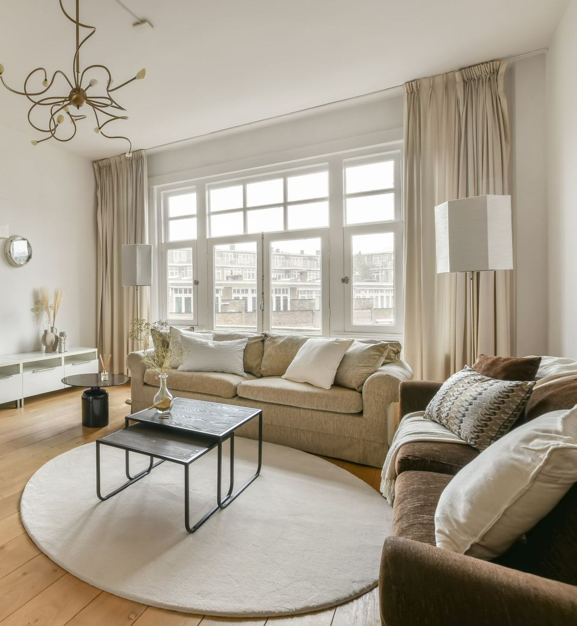 Living room with beige sofa, brown armchair, round rug, and window with curtains. Living room with beige sofa, brown armchair, round rug, and window with curtains.
