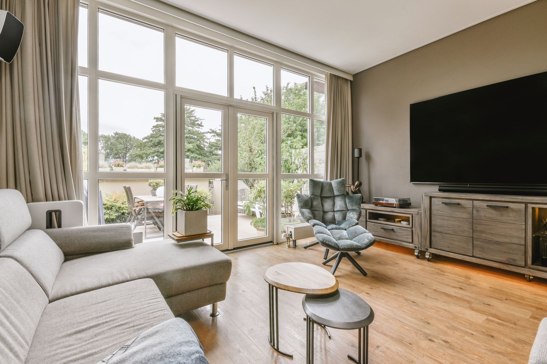 Living room with gray sofa, large TV, windows, and small round coffee tables.