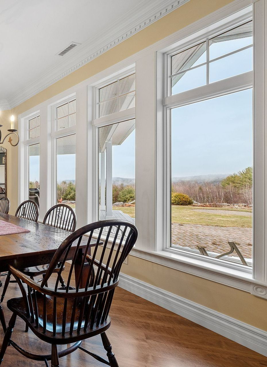 Dining room with wooden table and chairs, large windows overlooking a grassy landscape.