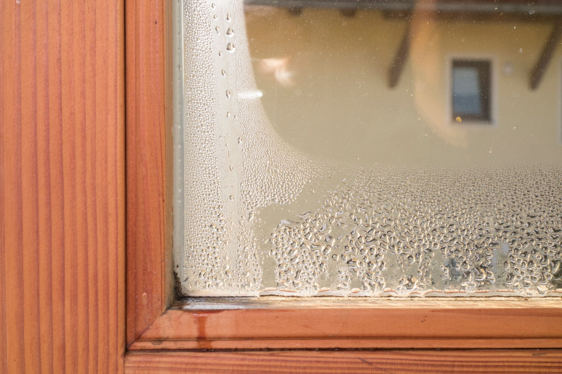 Close-up of a window with condensation. Wooden frame, exterior light-colored wall reflected in the glass. Close-up of a window with condensation. Wooden frame, exterior light-colored wall reflected in the glass.