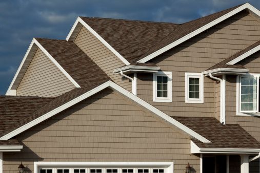 Tan and brown house with white trim against a cloudy sky.