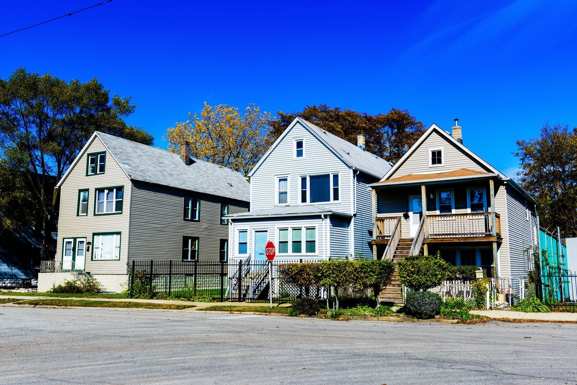 Row of three houses, varying colors, against a clear blue sky. Two-story buildings with pitched roofs and visible front doors. Row of three houses, varying colors, against a clear blue sky. Two-story buildings with pitched roofs and visible front doors.