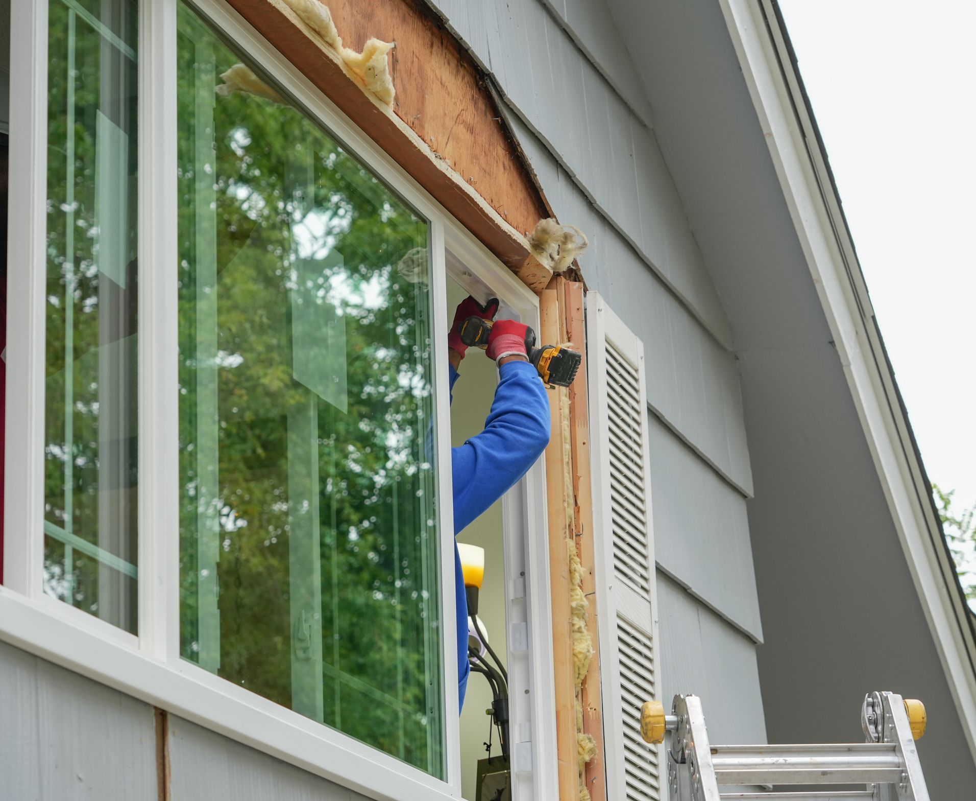 Person installing a window, using a drill on a house exterior. Person installing a window, using a drill on a house exterior.