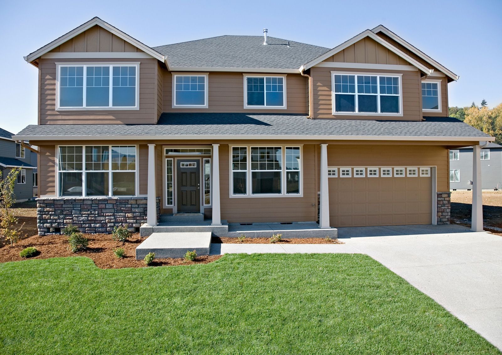 Two-story house with brown siding, a dark roof, a stone accent, and a green lawn.