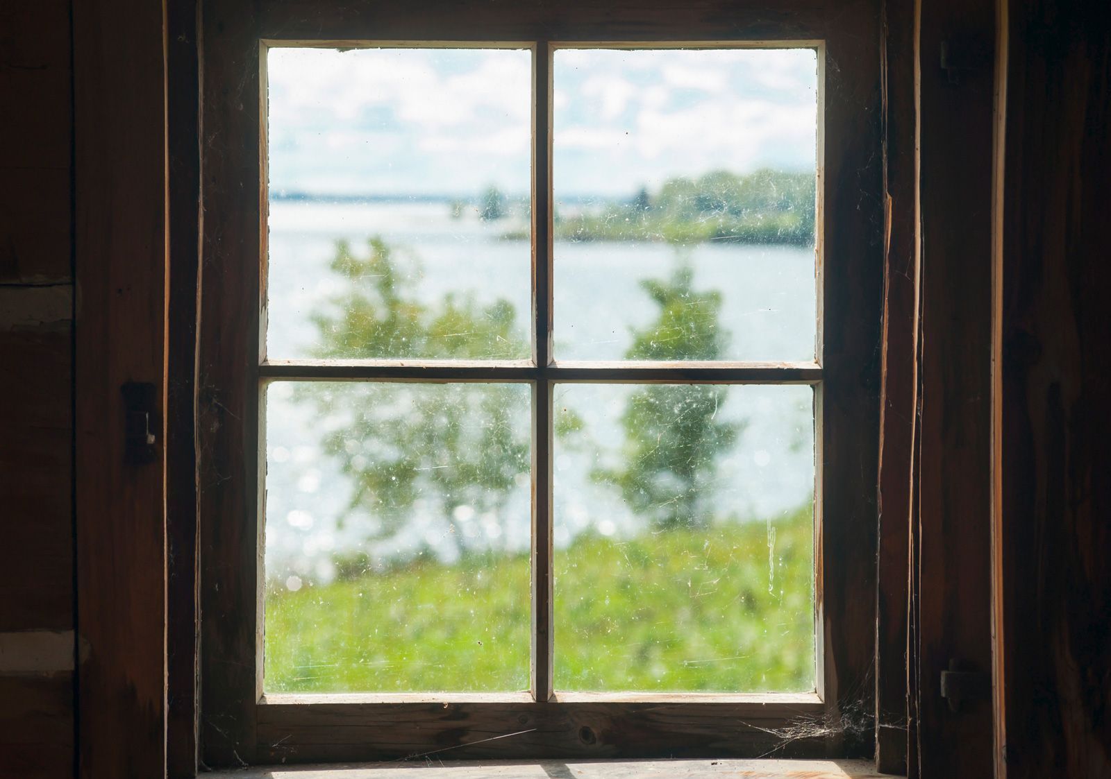 Wooden-framed window view of lake and trees on a sunny day.