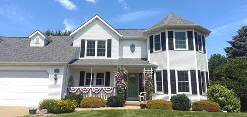 White two-story house with a rounded side, black shutters, and a blue door, against a clear sky.