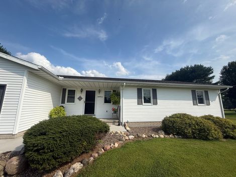 White house with black roof and shutters, green lawn, blue sky.