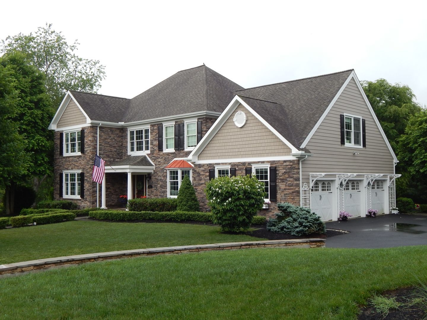 Two-story brick house with a dark roof, white trim, and a three-car garage on a well-manicured lawn.