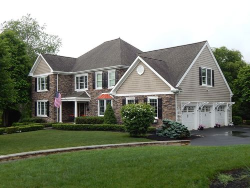 Two-story brick house with a dark roof, white trim, and a three-car garage on a well-manicured lawn.