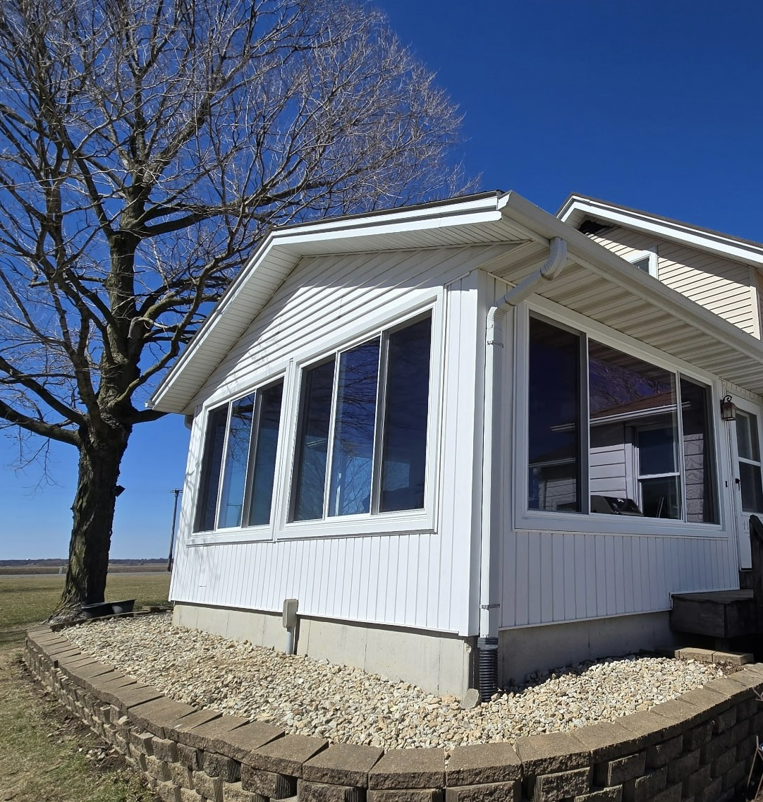 White house with large windows, leafless tree, gravel bed, and blue sky.